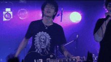 a man in a black shirt with a flower on it is playing a guitar and singing into a microphone