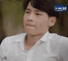 a young man in a white shirt is sitting down and making a funny face .