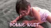 a little girl is crawling on the sand with the words `` bonne nuit '' written on it .