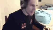 a man is sitting in a chair in front of a bed and making a funny face .