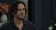 a man with a beard wearing a blue shirt is looking at the camera .
