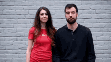 a man and a woman standing next to each other in front of a brick wall .