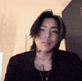 a man with long hair and a tattoo on his neck is wearing a black jacket .