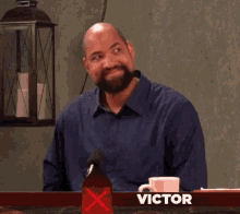 a man with a beard is smiling in front of a red sign that says victor on it