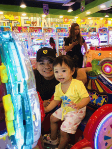 a little girl sits next to a man in an arcade with a sign above them that says is fun