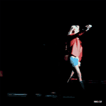 a woman in a red jacket stands on a stage holding a microphone