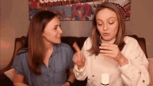 two women are sitting on a couch and one of them is holding a bottle