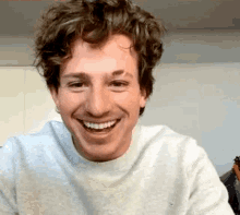 a man with curly hair is smiling for the camera while wearing a gray sweater .