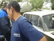 a man in a blue shirt is standing next to a car