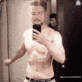 a shirtless man is taking a selfie with his cell phone in a mirror .