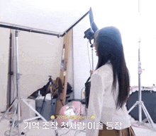 a woman in a white shirt and brown skirt stands in a room with korean writing on the wall