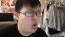 a man wearing glasses is making a funny face in front of a closet full of clothes .