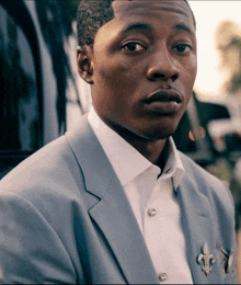 a man in a suit has a fleur de lis brooch on his pocket square