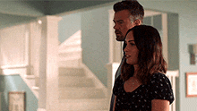a man and a woman are standing next to each other in a room in front of stairs .