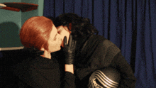 a man and woman are kissing in front of a blue curtain