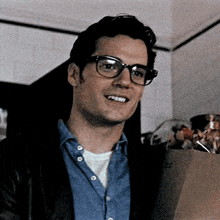 a man wearing glasses and a denim shirt is smiling .