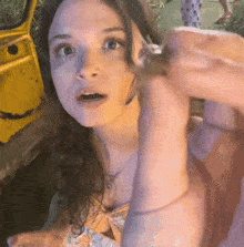 a woman in a yellow top is holding a small animal in her hand