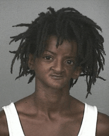 a woman with dreadlocks and a white tank top makes a funny face