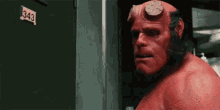 a red monster with horns is standing in front of a door .