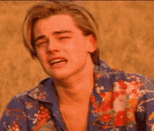a young man in a floral shirt is crying while standing on a beach .