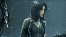 a woman with long black hair is wearing a black jacket with gold trim