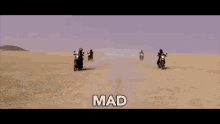 a group of people are riding motorcycles in the desert and the word mad is visible in the corner .