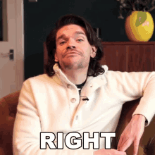 a man in a white sweater is sitting on a couch with the word right written on his chest