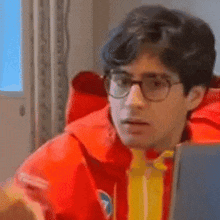 a man wearing glasses and a red jacket is sitting in front of a laptop computer