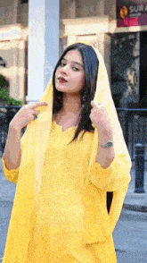 a woman wearing a yellow dress and a yellow scarf is standing on a street .