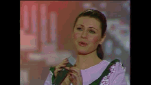 a woman is singing into a microphone while wearing a pink top