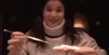 a woman in a turtleneck sweater is holding a fork and smiling while eating food .