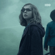 a woman wearing glasses and a purple jacket is standing in a foggy room .