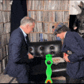 two men are sitting on a couch in front of a bookshelf