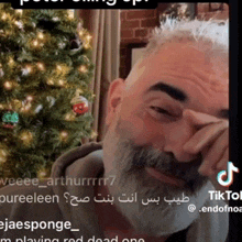a man with a beard covering his face with his hand in front of a christmas tree