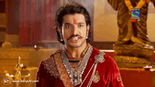 a man with a mustache is wearing a red velvet outfit and pearls .