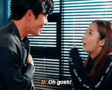 a man and a woman are standing next to each other in front of a window and talking .