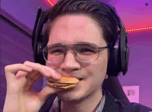 a man wearing glasses and headphones is eating a piece of food .