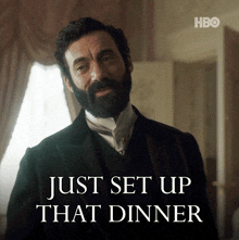 a man with a beard is standing in front of a sign that says " just set up that dinner "