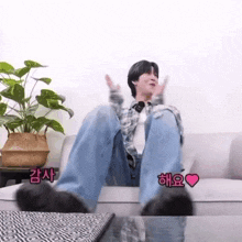 a man is sitting on a couch with his legs crossed and a plant behind him