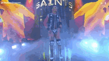 a wrestler is standing in front of a sign that says saints on it .