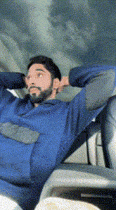 a man with a beard is sitting in a car with his arms behind his head