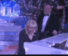 a man in a tuxedo is standing next to a woman playing a piano in front of a pink police sign