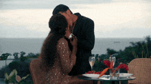 a man and a woman are kissing at a table with wine glasses