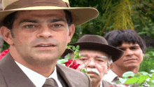 a man in a hat stands next to two other men in suits