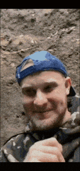 a man wearing a blue hat and a camouflage jacket smiles