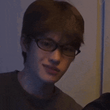 a young man wearing glasses is smiling and looking at the camera in a dark room .