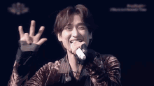 a young man is singing into a microphone with his hand in the air