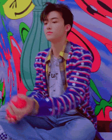 a young man is sitting on the floor holding a red ball in front of a colorful painting .