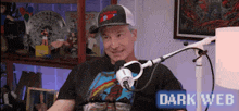 a man wearing a hat is sitting in front of a microphone with the words dark web below him .