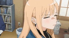 a girl with blonde hair is sitting in front of a bookshelf and a trash can